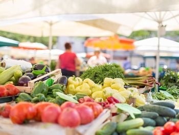 Farmers' food market stall with variety of organic vegetable. Vendor serving and chating with customers.